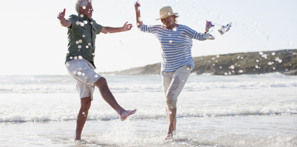 Retired couple kicking water on a beach. 
