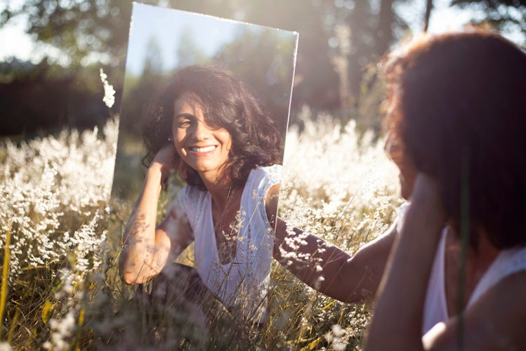 Woman looking in a mirror in the sunlight in a field
