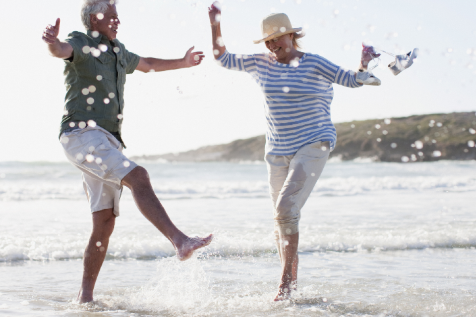 Retired couple kicking water on a beach. 