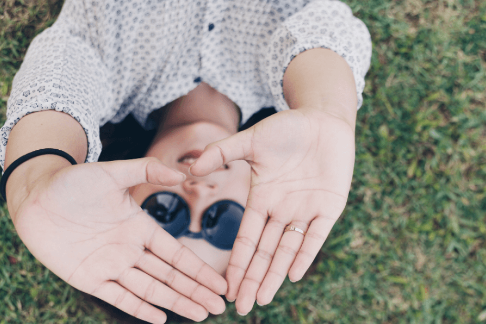 Person laying in the grass forming a heart shape with their hands